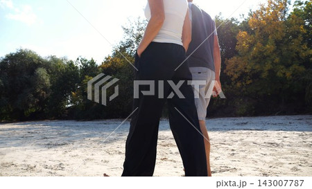 Happy pair going along coast at sunny day. Romantic couple holding hands of each other and walking on sandy beach. Lovers spending time together at resort. Concept of summer vacation or holiday 143007787