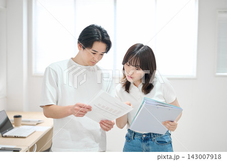 オフィスで書類をチェックする若い男女 オフィスで書類をチェックする若い男女 143007918