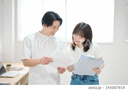 オフィスで書類をチェックする若い男女 オフィスで書類をチェックする若い男女 143007919