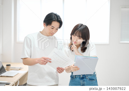 オフィスで書類をチェックする若い男女 オフィスで書類をチェックする若い男女 143007922
