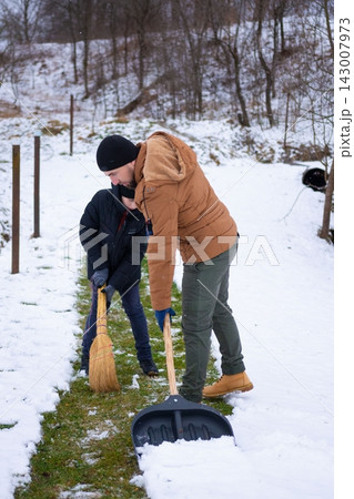 Father and son teamwork: clearing snow from a pathway using a shovel and broom. Winter cleanup. 143007973