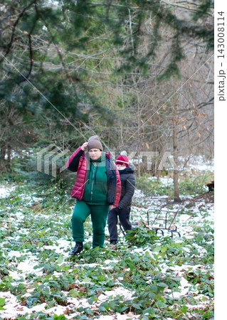 A woman and child trek through a snowy woodland, pulling a sled behind them. Winter adventure in the woods. A woman and child trek through a snowy woodland, pulling a sled behind them. Winter adventure in the woods. 143008114