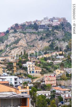 Distant coastline and Ionian Sea appear through fog beyond Castelmola village overlook in eastern Sicily. Concept of dramatic coastal panorama and moody mountain top viewpoint photography. 143008221