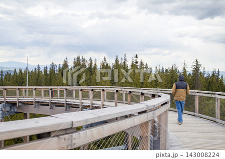 Man walking on panoramic wooden platform with dramatic mountain landscape in High Tatras near Zakopane. Solo travel, outdoor exploration and scenic tourism lifestyle concept. Man walking on panoramic wooden platform with dramatic mountain landscape in High Tatras near Zakopane. Solo travel, outdoor exploration and scenic tourism lifestyle concept. 143008224