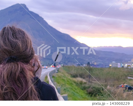 Close view of female traveler looking at sunset road landscape in Sicily near Palermo. Emotional travel moment, Mediterranean freedom, scenic journey and vacation inspiration concept. Close view of female traveler looking at sunset road landscape in Sicily near Palermo. Emotional travel moment, Mediterranean freedom, scenic journey and vacation inspiration concept. 143008229