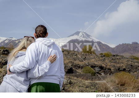 Couple standing and embracing while looking at Mount Etna volcano landscape. Travel, relationship and shared moments concept, enjoying scenic view in early spring nature. 143008233