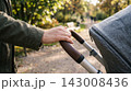 Close-up macro shot of a mother's elegantly manicured hand resting on the leather handle of a modern stroller in a cafe. 143008436