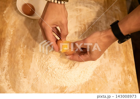 Hands breaking egg into flour well on wooden table Hands breaking egg into flour well on wooden table 143008973