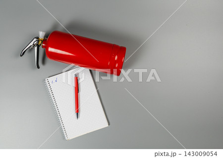 Fire extinguisher placed on a gray surface with a notepad and pen Fire extinguisher placed on a gray surface with a notepad and pen 143009054