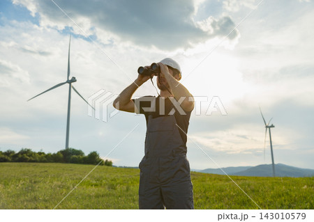 A man in work clothes surveys a field with wind turbines under a cloudy sky, symbolizing renewable energy and observation 143010579