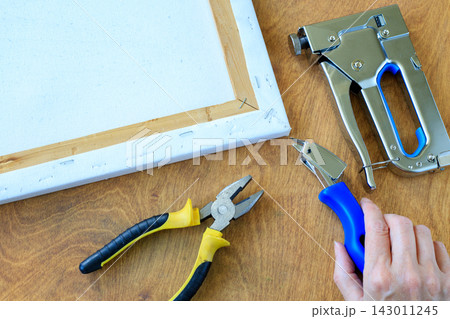 Canvas Stretching Process with Stapler, Pliers, and Remover Tool on Wooden Table. Art Framing Concept Canvas Stretching Process with Stapler, Pliers, and Remover Tool on Wooden Table. Art Framing Concept 143011245