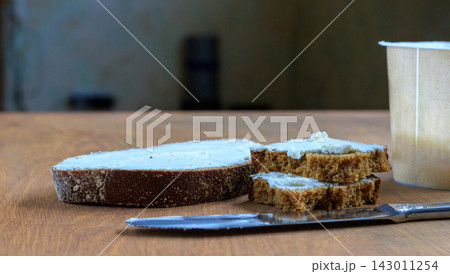 Rye Bread Sandwiches with Soft White Spread, Knife and Dairy Container on Wooden Surface 143011254