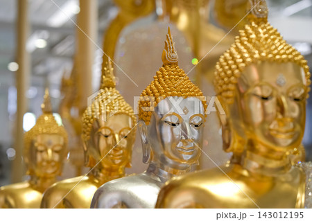 Multiple golden and silver Buddha statues sit in a neat row. These serene figures embody peace and spiritual devotion. Multiple golden and silver Buddha statues sit in a neat row. These serene figures embody peace and spiritual devotion. 143012195