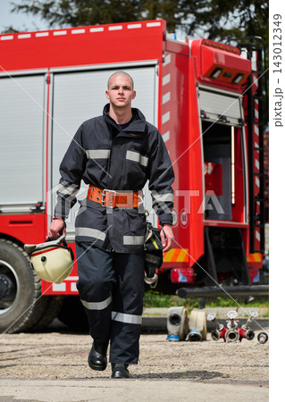 Firefighter Walking Toward Camera With Helmet Near Red Fire Truck And Rescue Equipment 143012349