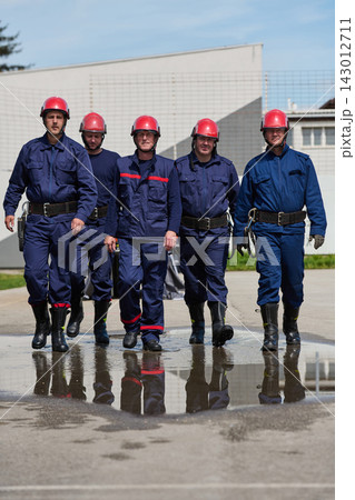 Firefighters Team Walking Together in Red Helmets and Blue Uniforms With Reflection on Wet Pavement Firefighters Team Walking Together in Red Helmets and Blue Uniforms With Reflection on Wet Pavement 143012711