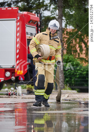 Firefighter Carrying Rolled Fire Hose Near Red Fire Truck During Wet Emergency Response Training Firefighter Carrying Rolled Fire Hose Near Red Fire Truck During Wet Emergency Response Training 143012794