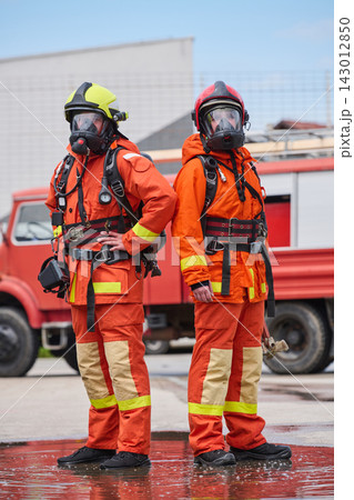 Two Firefighters in Orange Protective Suits With Respirators Standing in Front of Fire Truck Two Firefighters in Orange Protective Suits With Respirators Standing in Front of Fire Truck 143012850