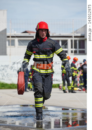 Firefighter Running in Training Drill Carrying Hose on Wet Pavement With Team in Background Firefighter Running in Training Drill Carrying Hose on Wet Pavement With Team in Background 143012975