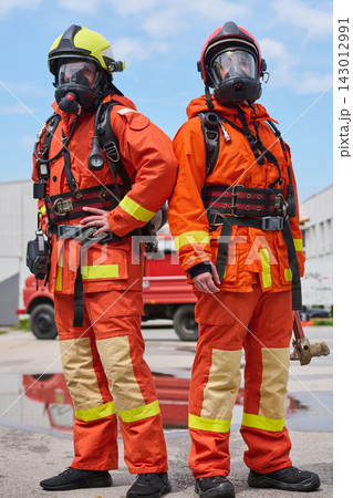 Two Firefighters in Full Protective Gear With Masks and Helmets Standing Confidently by Fire Truck 143012991