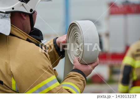 Firefighter Holding Rolled Fire Hose During Emergency Drill With Protective Gear And Helmet Firefighter Holding Rolled Fire Hose During Emergency Drill With Protective Gear And Helmet 143013237