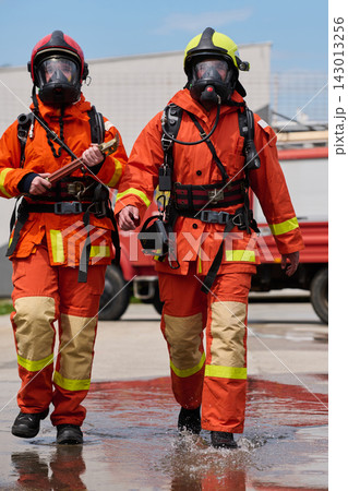 Two Firefighters In Orange Protective Gear Walking With Masks And Equipment Near Fire Truck Two Firefighters In Orange Protective Gear Walking With Masks And Equipment Near Fire Truck 143013256