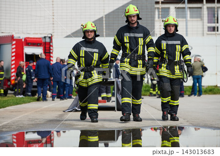 Three Firefighters Walking Toward Camera in Gear With Firetruck and Crew at Emergency Scene 143013683
