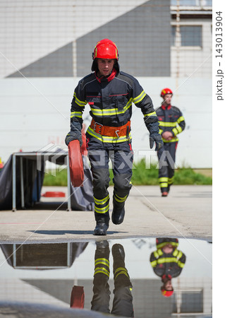 Firefighter Running With Hose During Training Drill In Protective Gear Reflecting In Puddle Firefighter Running With Hose During Training Drill In Protective Gear Reflecting In Puddle 143013904