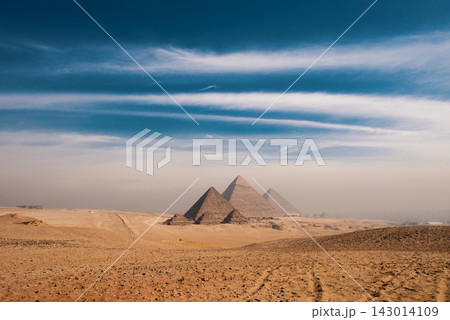 Ancient giza pyramids panoramic wide landscape across sandy desert plateau under dramatic two tone blue sky and hazy golden horizon Egypt travel 143014109