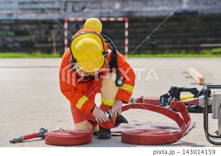 Firefighter Preparing Fire Hose and Wearing Helmet During Emergency Training Drill On Pavement 143014159
