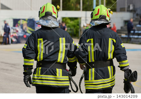 Two Firefighters in Protective Gear Walking Together Holding Rope Demonstrating Teamwork and Safety 143014209