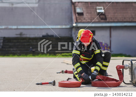 Firefighter Preparing Hose During Outdoor Training Exercise Wearing Protective Gear And Red Helmet Firefighter Preparing Hose During Outdoor Training Exercise Wearing Protective Gear And Red Helmet 143014212