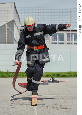 Firefighter Balancing on Beam While Carrying Hose During Outdoor Training Exercise With Helmet And Gear Firefighter Balancing on Beam While Carrying Hose During Outdoor Training Exercise With Helmet And Gear 143014252