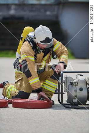 Firefighter In Full Protective Gear Kneeling to Prepare Hose and Pump During Training Exercise Firefighter In Full Protective Gear Kneeling to Prepare Hose and Pump During Training Exercise 143014283
