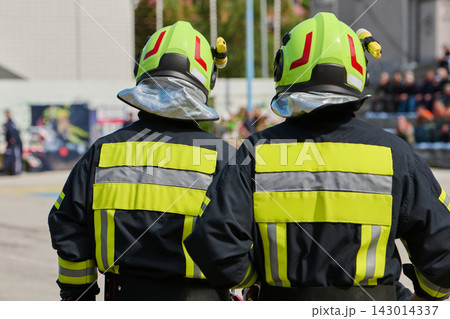 Two Firefighters in High-Visibility Helmets and Reflective Jackets Standing at Emergency Scene Two Firefighters in High-Visibility Helmets and Reflective Jackets Standing at Emergency Scene 143014337