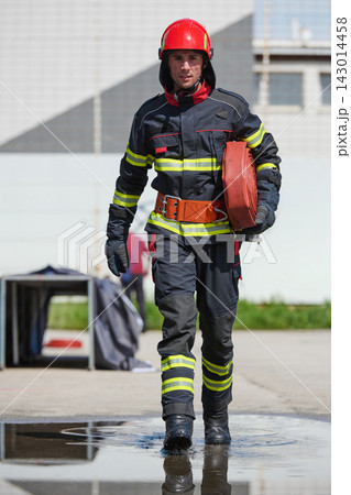 Firefighter In Full Gear Carrying Fire Hose Walking Through Puddle During Emergency Response Firefighter In Full Gear Carrying Fire Hose Walking Through Puddle During Emergency Response 143014458