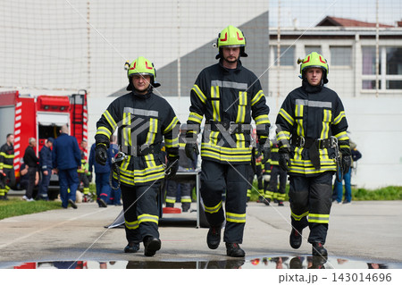 Three Firefighters Walking Confidently in Protective Gear With Fire Truck and Crew in Background 143014696