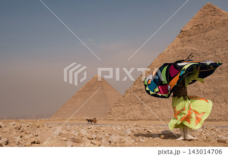 Tanoura dancer in vivid multicolored patchwork costume spinning dramatically before the iconic twin Giza pyramids on the arid plateau in Egypt with 143014706