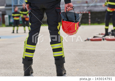 Firefighter Holding Red Helmet During Training Drill With Team In High-Visibility Uniform 143014791