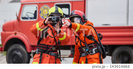 Firefighters in Protective Gear Using Thermal Imaging Camera Next to Red Fire Truck During Rescue Operation Firefighters in Protective Gear Using Thermal Imaging Camera Next to Red Fire Truck During Rescue Operation 143014868