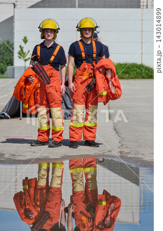 Two Firefighters Standing With Jackets and Helmets Beside Reflective Puddle During Training 143014899