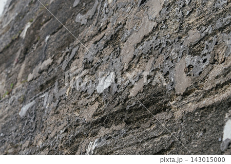 A close view shows the rough porous texture of a weathered stone wall. The gray and brown rocky surface creates a natural abstract background. A close view shows the rough porous texture of a weathered stone wall. The gray and brown rocky surface creates a natural abstract background. 143015000