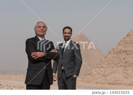 Two multigenerational Middle Eastern male executives in formal business suits posing with authority before the monumental Giza pyramids ideal for MENA 143015035