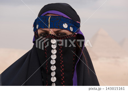 Close up portrait of an egyptian woman in traditional bedouin niqab adorned with silver Eye of Horus coins and blue beaded headband set against a soft Close up portrait of an egyptian woman in traditional bedouin niqab adorned with silver Eye of Horus coins and blue beaded headband set against a soft 143015161