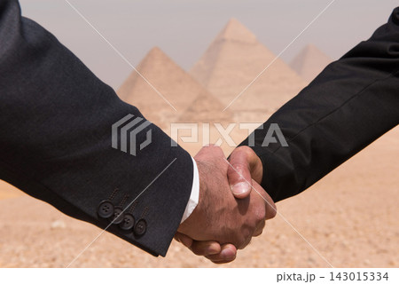 Two business executives in dark suits sealing an international deal with a firm handshake against the iconic Giza pyramids in Egypt ideal for global Two business executives in dark suits sealing an international deal with a firm handshake against the iconic Giza pyramids in Egypt ideal for global 143015334