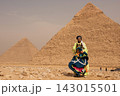 Tanoura costume male performer holds colorful spinning skirt mid swirl standing before the Great Pyramids of Giza on the sandy Egyptian desert plateau 143015501