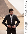 Focused Arab executive in dark suit and tie adjusting jacket button on Giza sandy plateau with iconic Great Pyramid silhouette behind him ideal for 143015517