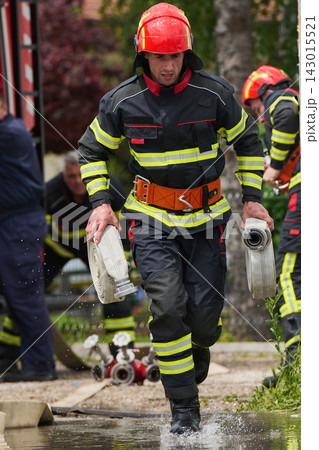 Firefighter Running With Water Hoses During Emergency Response Training In Protective Gear Firefighter Running With Water Hoses During Emergency Response Training In Protective Gear 143015521
