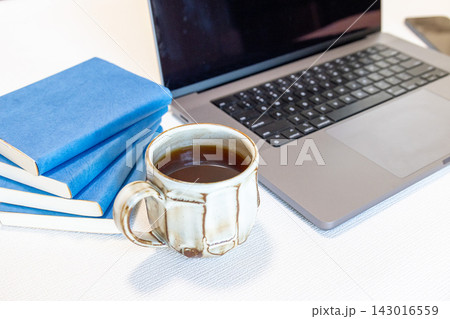 ノートパソコンとマグカップに入ったコーヒーと青い本 ノートパソコンとマグカップに入ったコーヒーと青い本 143016559