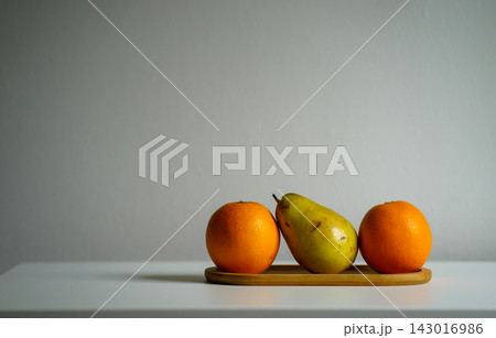 Two oranges and a green pear sit on a wooden board. Concept of fruit, nutrition, freshness, healthy eating, simplicity, balance, still life and taste Two oranges and a green pear sit on a wooden board. Concept of fruit, nutrition, freshness, healthy eating, simplicity, balance, still life and taste 143016986