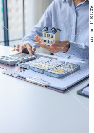 Businessman calculating budget, managing finances relating to housing or real estate holding miniature house with money and document on table Businessman calculating budget, managing finances relating to housing or real estate holding miniature house with money and document on table 143017056
